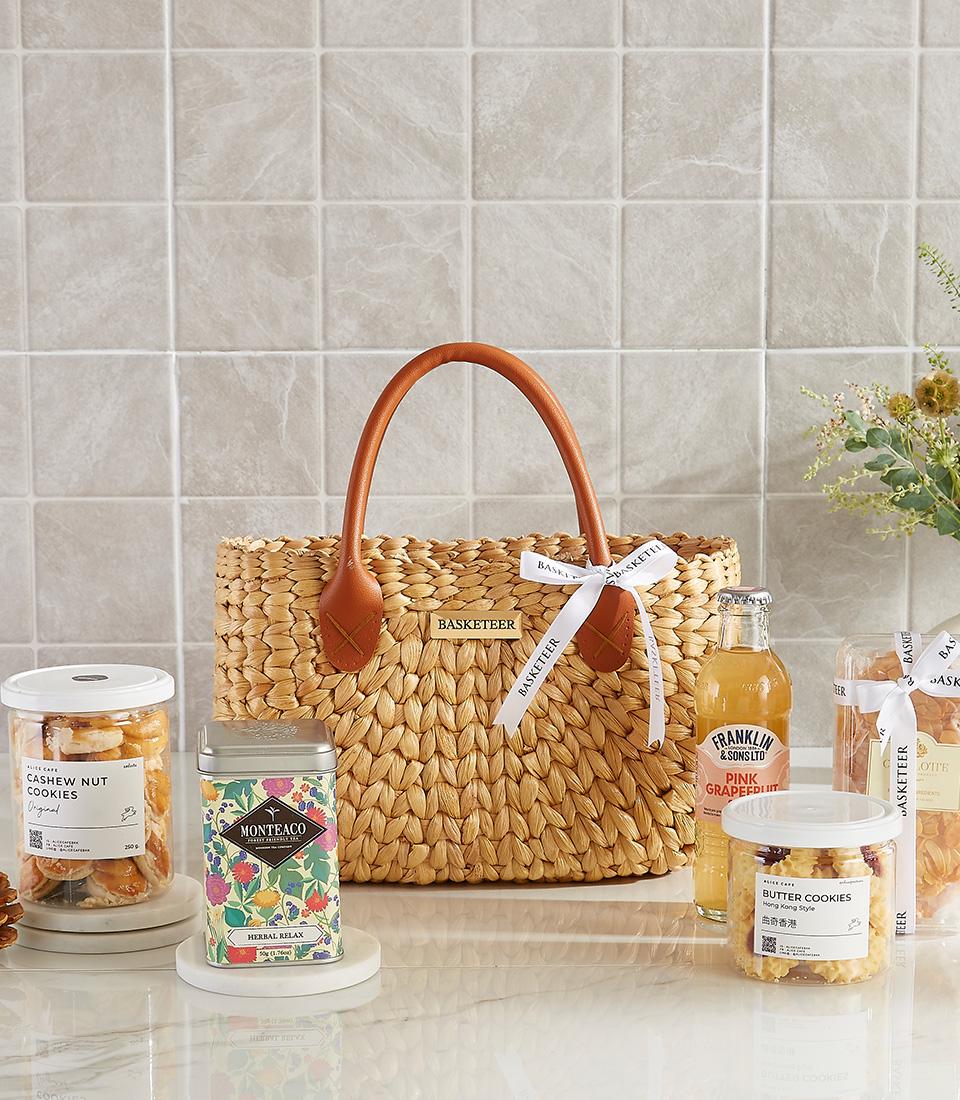 Woven straw gift bag with cashew cookies, herbal tea, pink grapefruit drink, and butter cookies for New Year wellness gifting