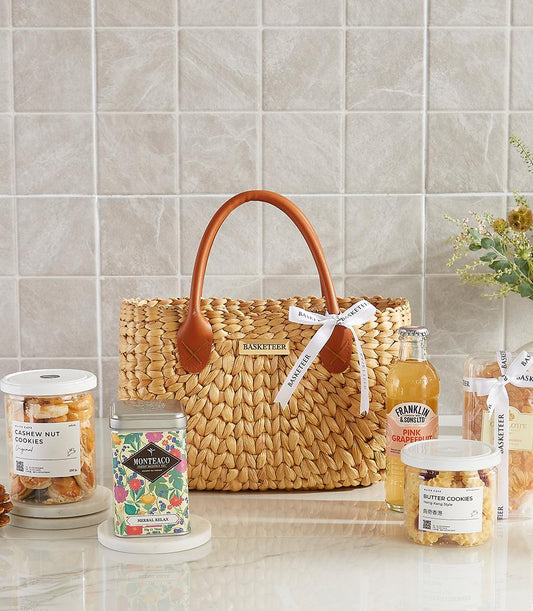 Woven straw gift bag with cashew cookies, herbal tea, pink grapefruit drink, and butter cookies for New Year wellness gifting