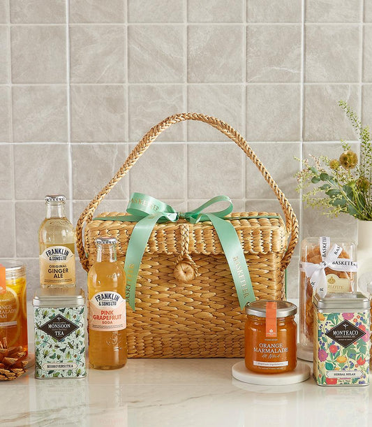 Woven picnic basket with gourmet sodas, artisan teas, marmalade, and Charlotte bakery treats for New Year wellness gifting