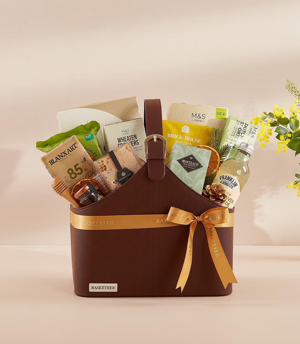 Luxury Loves brown leather gift basket with gourmet foods, honey, crackers, and gold ribbon bow for New Year gifting