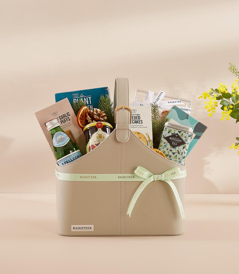 Premium savory and tea gift basket with sparkling water, Scottish cakes, and Monsoon tea, tied with green ribbon for New Year