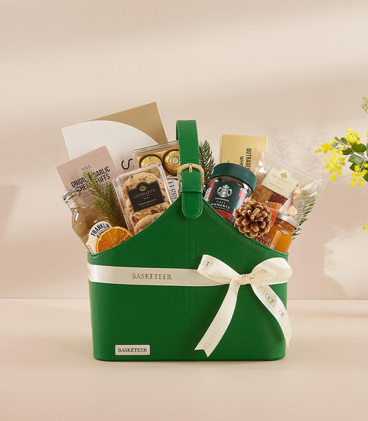 Green leather gift basket with gourmet treats, gold handle buckle, and white Basketeer ribbon for New Year gifting