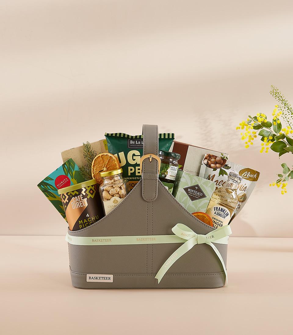 Grey faux leather gourmet gift basket with coffee, nuts, jam, and ginger ale, tied with green Basketeer ribbon for New Year