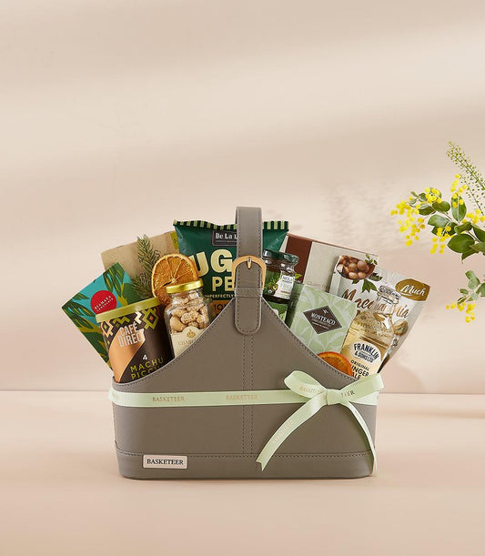 Grey faux leather gourmet gift basket with coffee, nuts, jam, and ginger ale, tied with green Basketeer ribbon for New Year