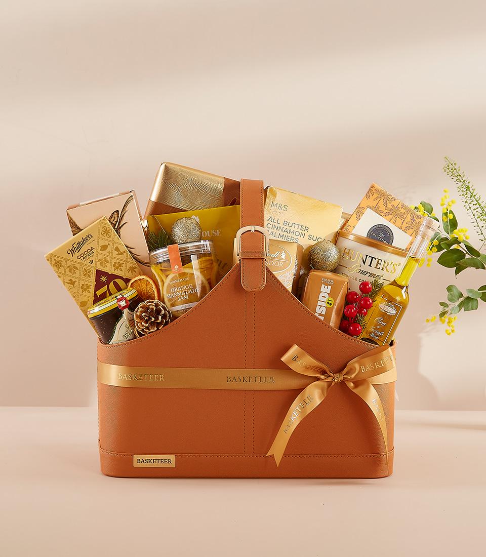 Burnt orange faux leather gift basket filled with gourmet chocolates, jam, palmiers, and olive oil, adorned with gold ribbon