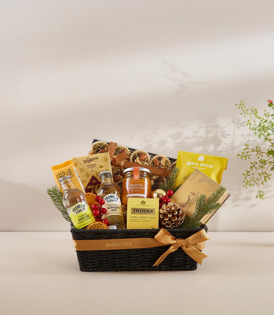 Premium gourmet gift basket with tea, marmalade, artisan pastries, and festive holiday trimmings in dark woven basket with
