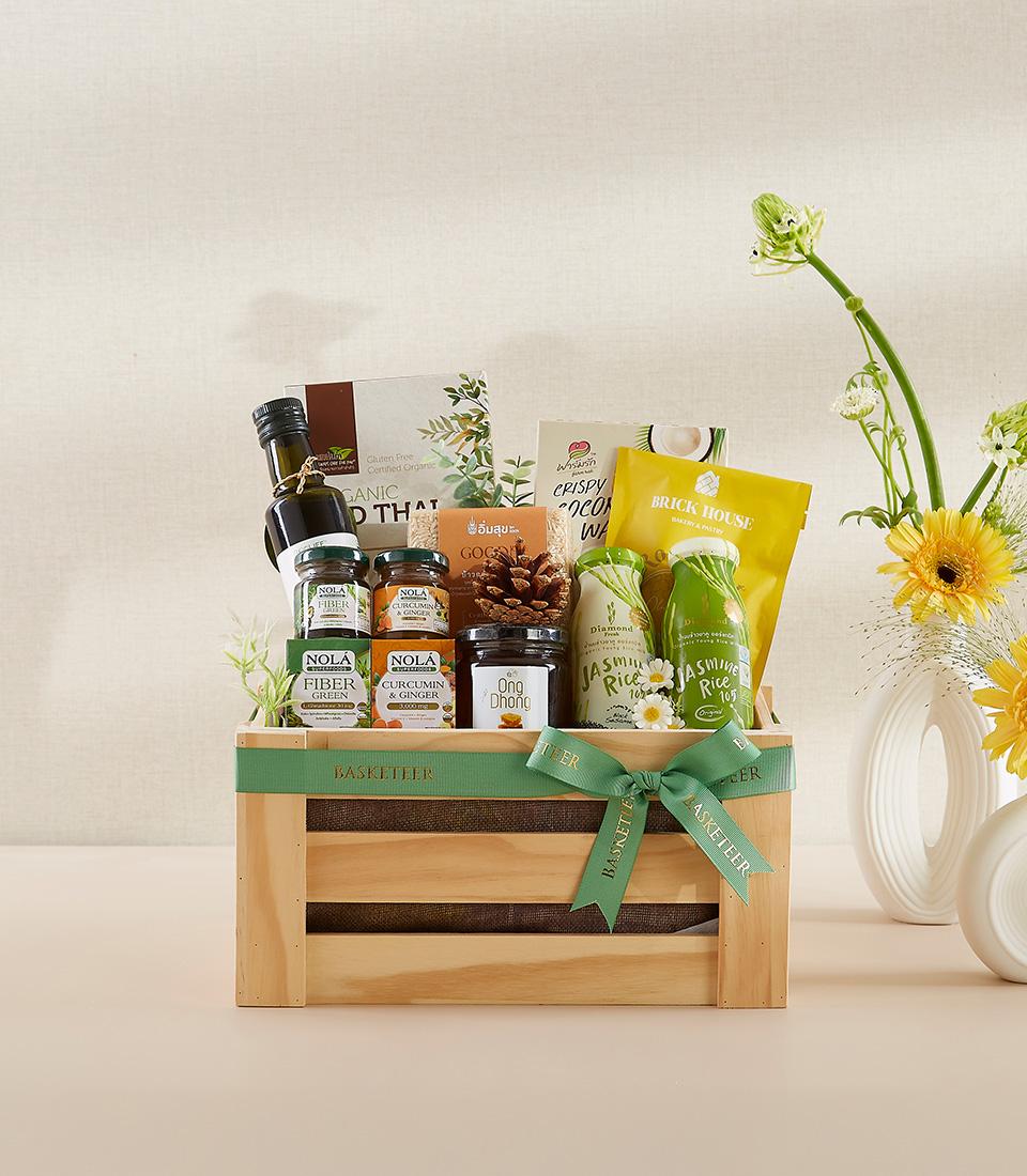 Organic wellness gift basket in natural wooden crate with green ribbon, filled with olive oil, supplements, and gourmet