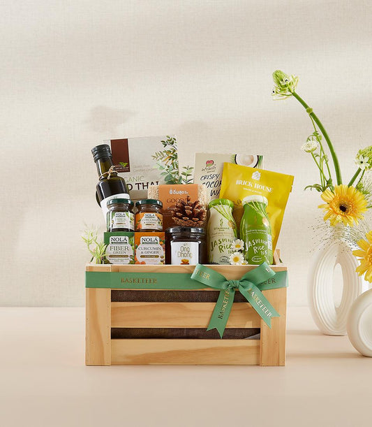 Organic wellness gift basket in natural wooden crate with green ribbon, filled with olive oil, supplements, and gourmet