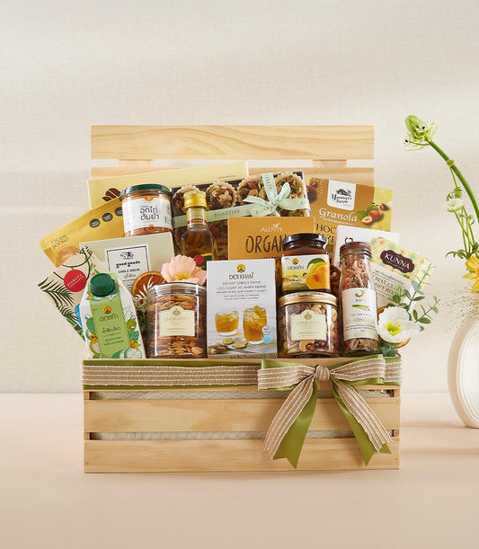 Wooden crate filled with organic gourmet items, nuts, oils, and wellness products tied with green ribbon for New Year gifting