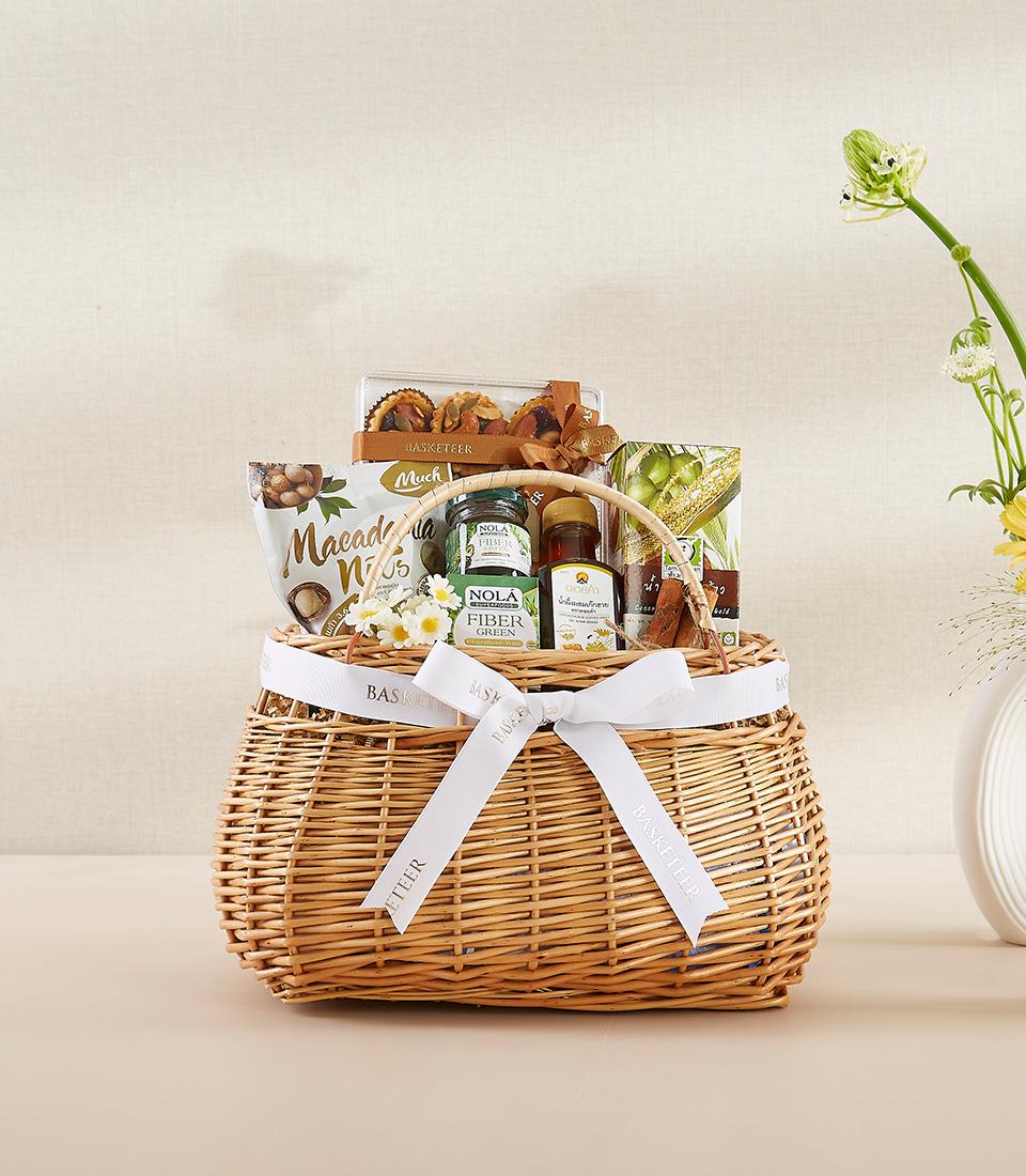 Premium natural nut and wellness gift basket with macadamia nuts, fiber supplements, and artisan tarts in woven wicker