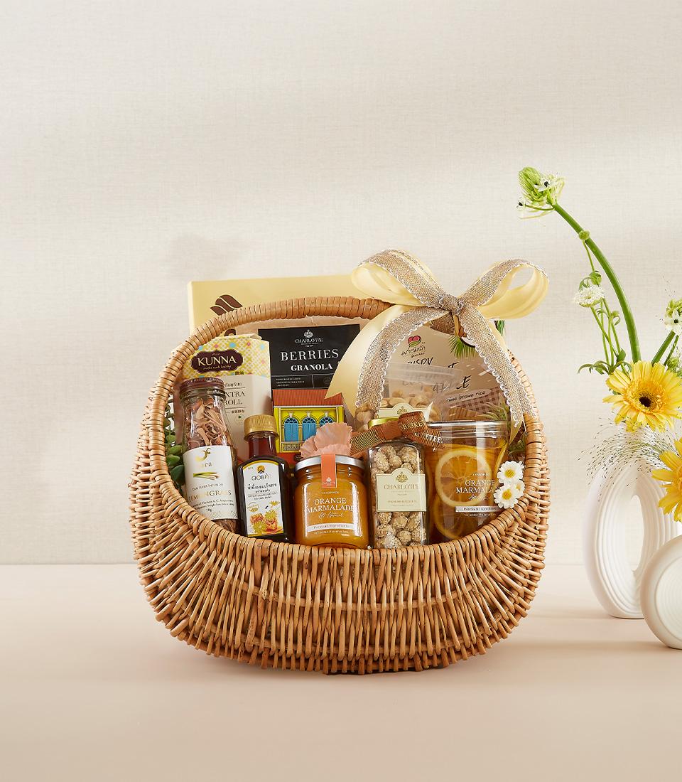 Light brown wicker gourmet basket with marmalade, granola, dried fruits, and honey, tied with yellow ribbon and fresh yellow