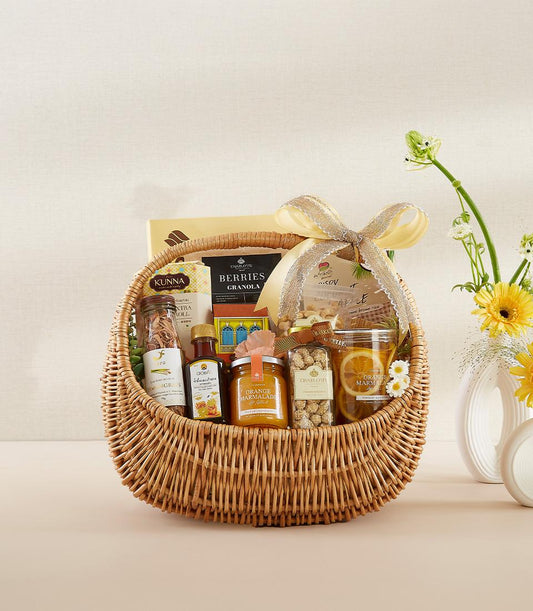 Light brown wicker gourmet basket with marmalade, granola, dried fruits, and honey, tied with yellow ribbon and fresh yellow