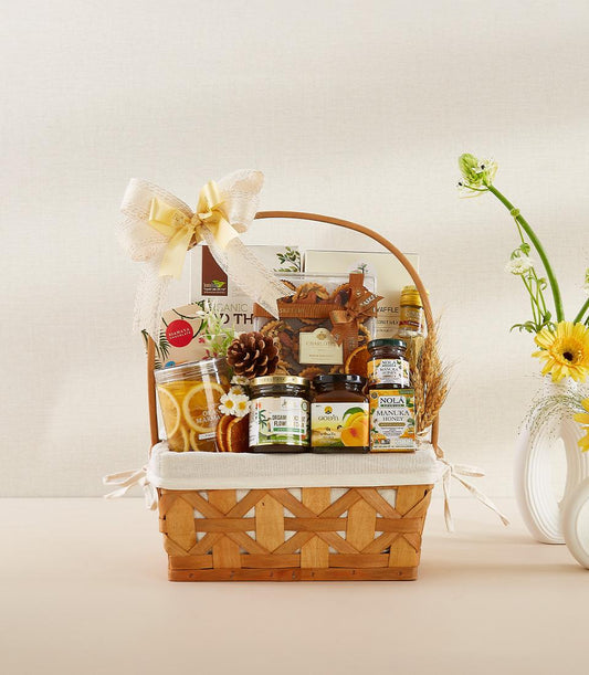 Woven light brown gourmet gift basket with Manuka honey, preserves, organic goods, and wheat accents tied with yellow bow