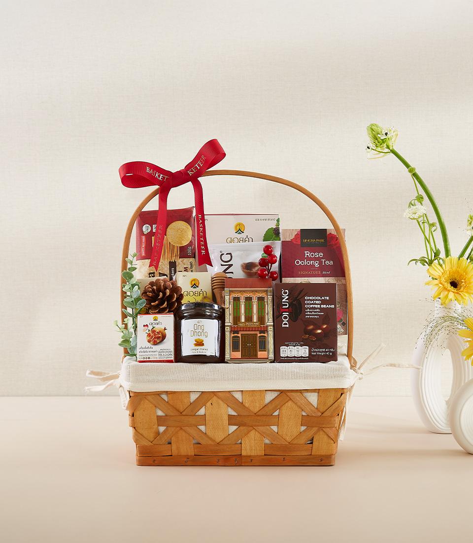 Woven wicker gift basket with rose oolong tea, chocolate coffee beans, honey, and festive decorative elements tied with red