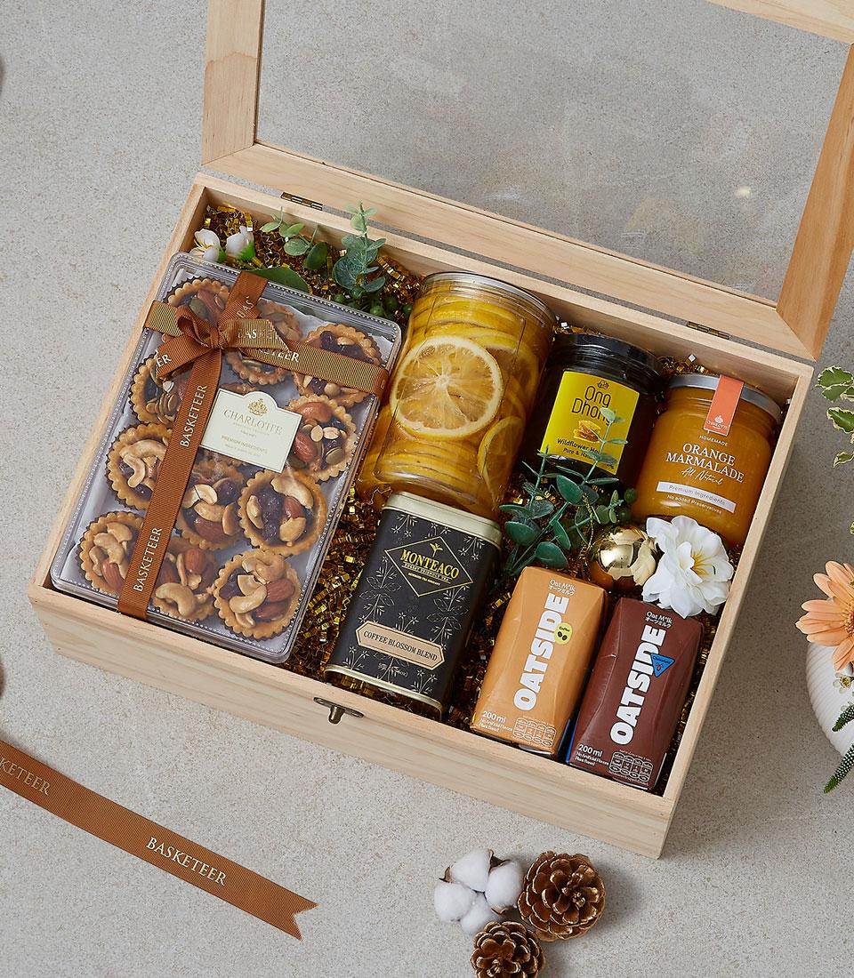 Wooden gift box filled with gourmet treats including nut tarts, honey, marmalade, coffee blend, and oat milk on gold