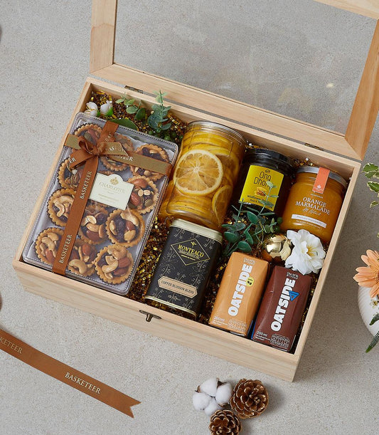 Wooden gift box filled with gourmet treats including nut tarts, honey, marmalade, coffee blend, and oat milk on gold