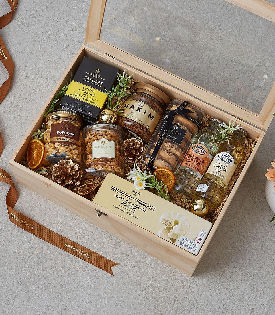 Wooden hamper box filled with gourmet treats, coffee, tea, snacks and beverages with natural decorative filler