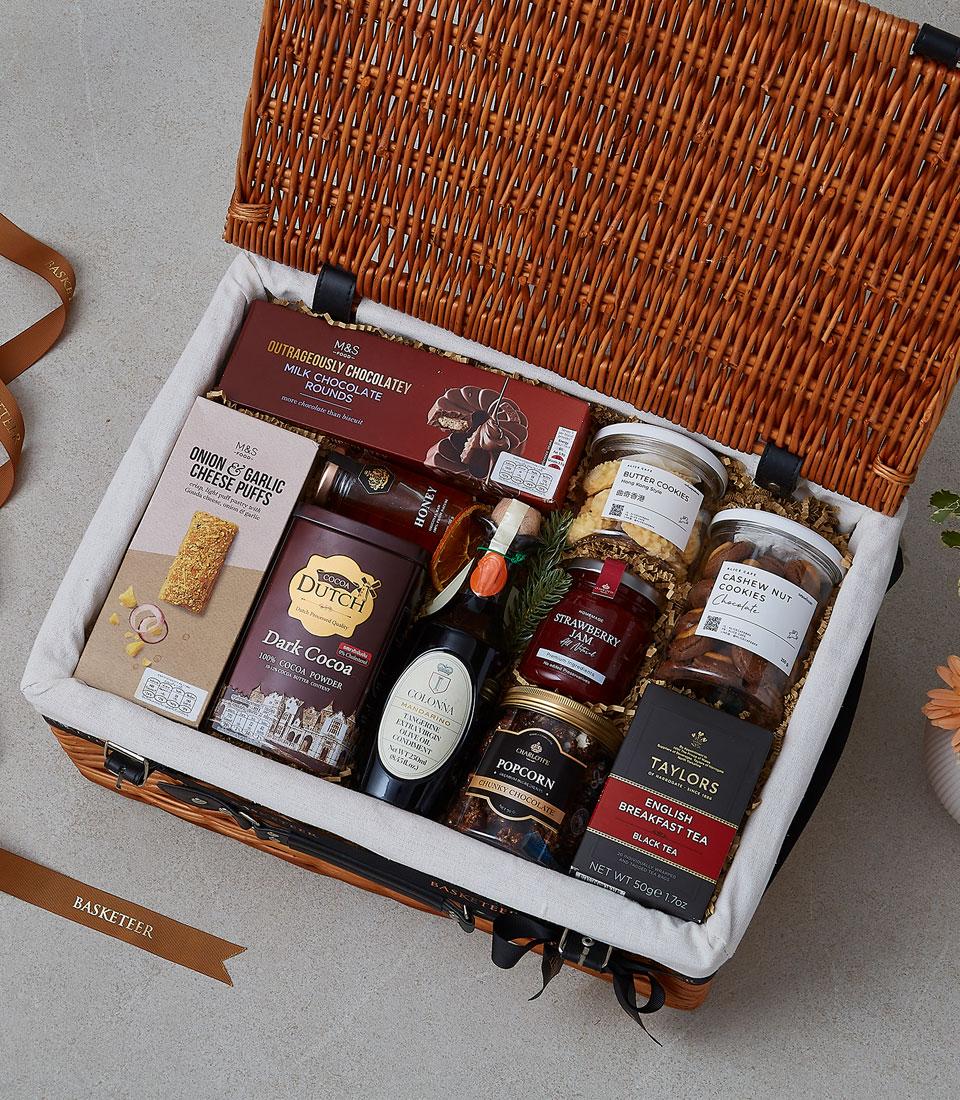 Wicker picnic hamper with gourmet treats, honey, olive oil, and artisan cookies in cream linen lining