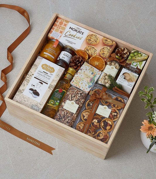 Wooden gift box filled with gourmet treats, cookies, honey, nuts, and dried fruits with festive ribbons and dried citrus