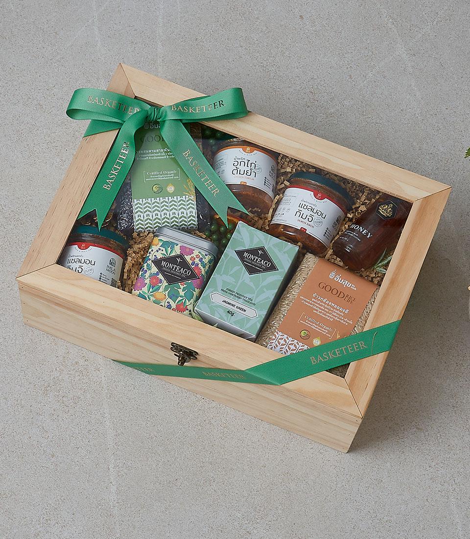 Luxury wooden gift box with artisan gourmet foods, honey, and specialty teas arranged on shredded paper with green Basketeer