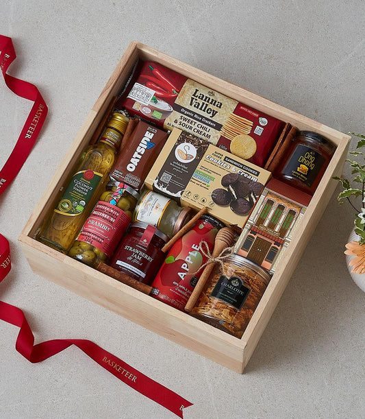 Wooden gift box filled with gourmet treats, coconut vinegar, honey, jams, and crackers with red ribbon