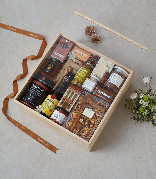 Wooden gourmet gift box with olives, honey, nuts, cookies, and artisan tarts tied with Basketeer ribbon