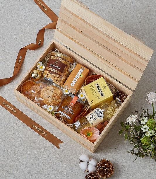 Wooden gift box with gourmet breakfast items, Earl Grey tea, oat milk, marmalade, and artisan cookies tied with brown ribbon