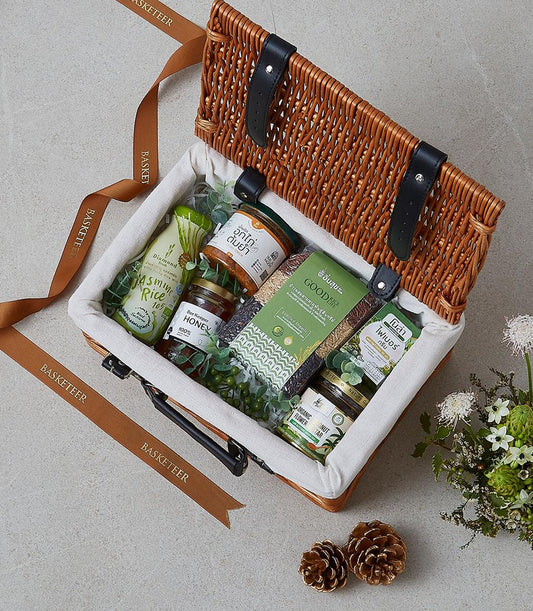 Wicker picnic basket with gourmet Thai pantry essentials, honey, and artisan ingredients on light grey background