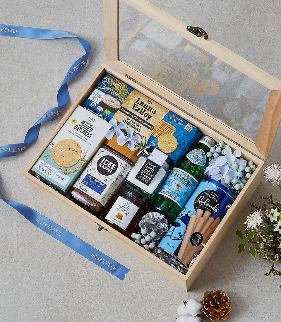 Wooden gift box filled with gourmet crackers, coffee, honey, mineral water and artisan treats with blue flowers