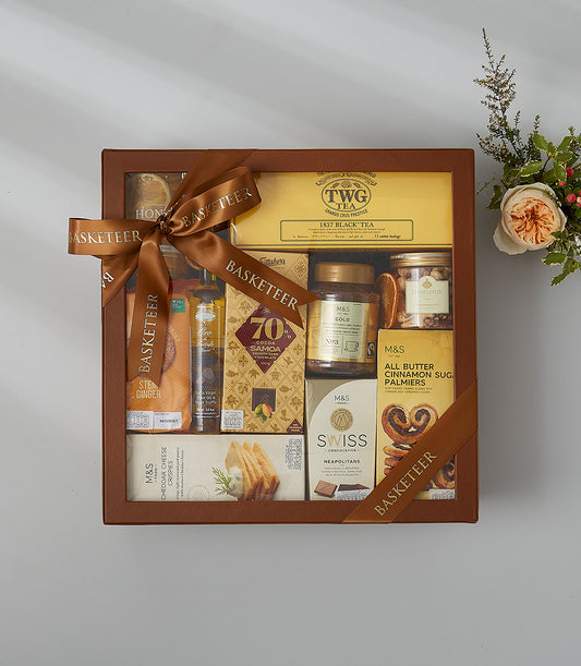 Brown leather gift box with gourmet treats, tea, coffee, chocolates, and nuts, tied with satin ribbon