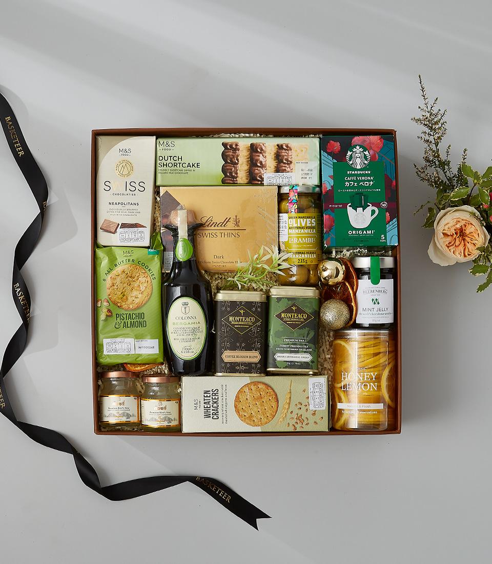 Deluxe gourmet hamper with artisan chocolates, shortbread, olives, and preserves in leather basket with fresh flowers