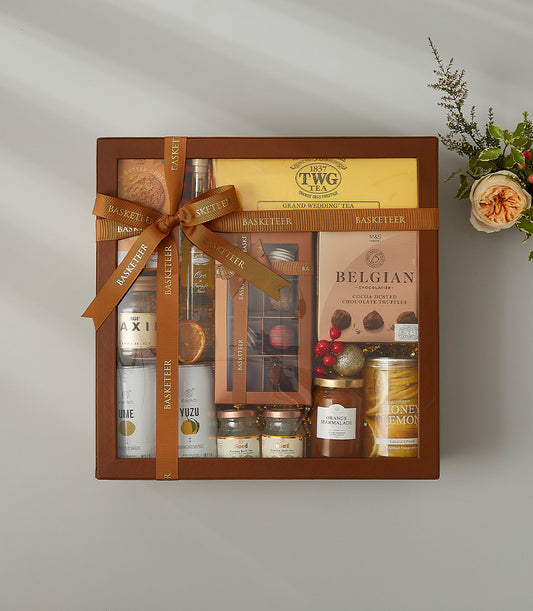Luxury tea and Belgian chocolate hamper in brown leather basket with gourmet jars, premium cakes, and fresh roses