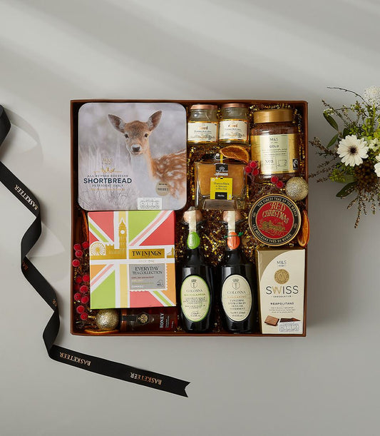 Luxury festive tea and treats hamper with shortbread, Twinings tea, honey, olive oil, and Swiss chocolates on gold shredded