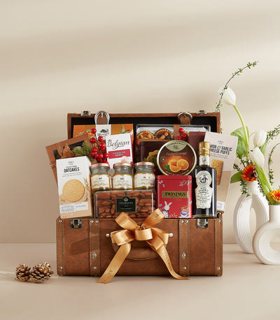 Luxury leather trunk hamper filled with gourmet chocolates, preserves, tea, and artisan foods with golden ribbon