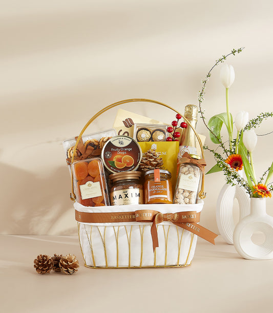 Premium gourmet gift basket with chocolates, coffee, and marmalade, styled with white tulips and festive pinecones for New