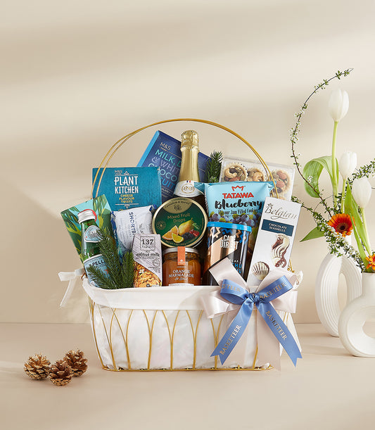 Luxury gourmet gift basket with sparkling wine, marmalade, and artisan treats in gold-trimmed white fabric liner, tied with
