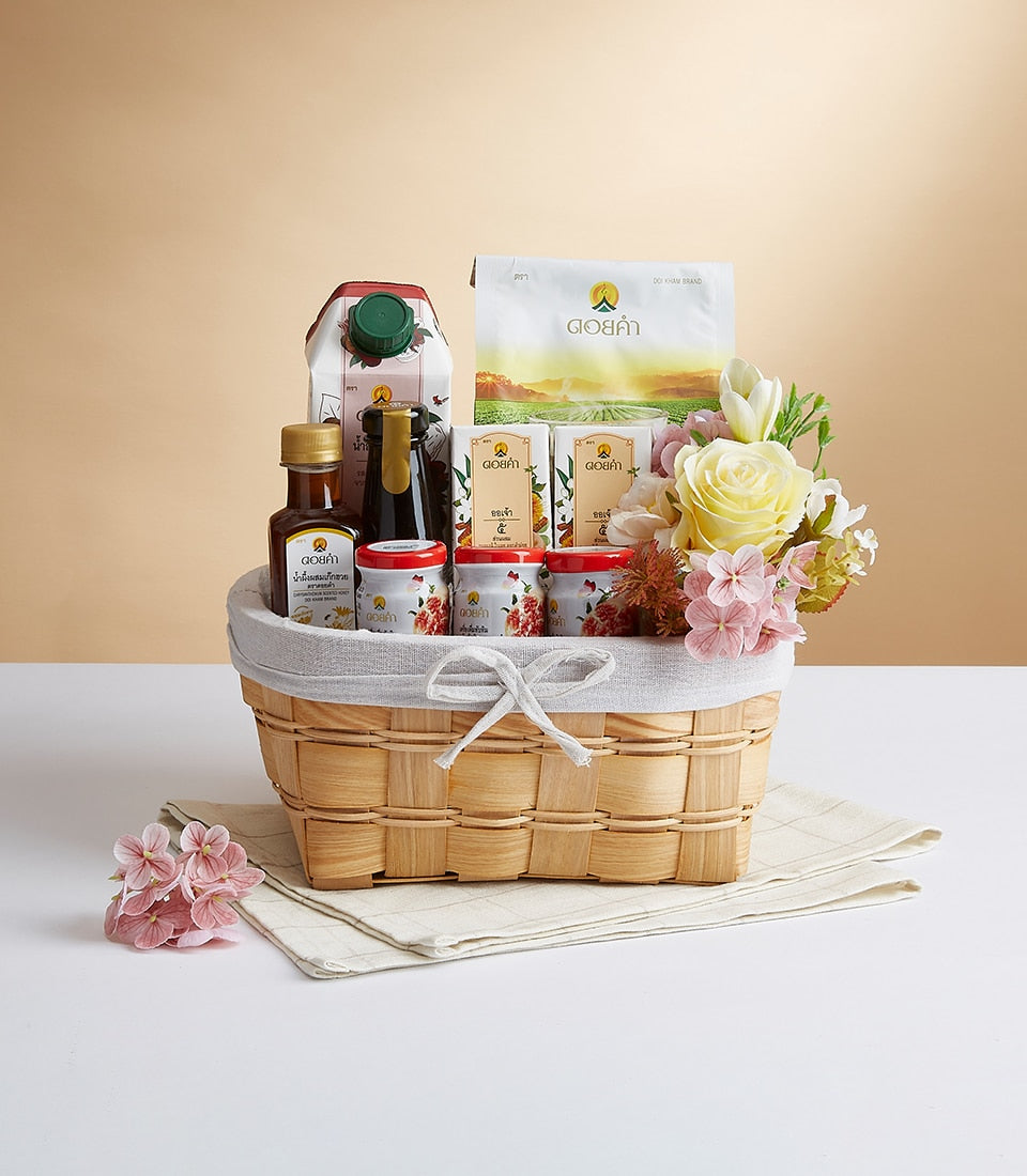 Woven gift basket filled with gourmet wellness products, yellow roses, and white tulips on checkered napkin