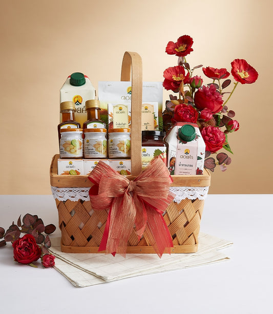 Woven wicker gift basket with Doi Kham gourmet foods, jarred preserves, and red ribbon bow beside festive artificial red