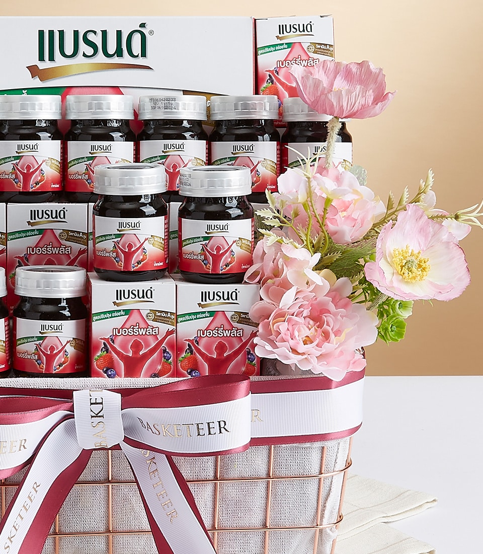 Berry Plus wellness drink gift basket with dark glass bottles, white and red packaging, woven cream basket with rose gold