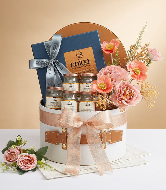 Luxury white gift box with rose gold bow, studded leather straps, premium bird's nest jars with gold lids, and peach pink