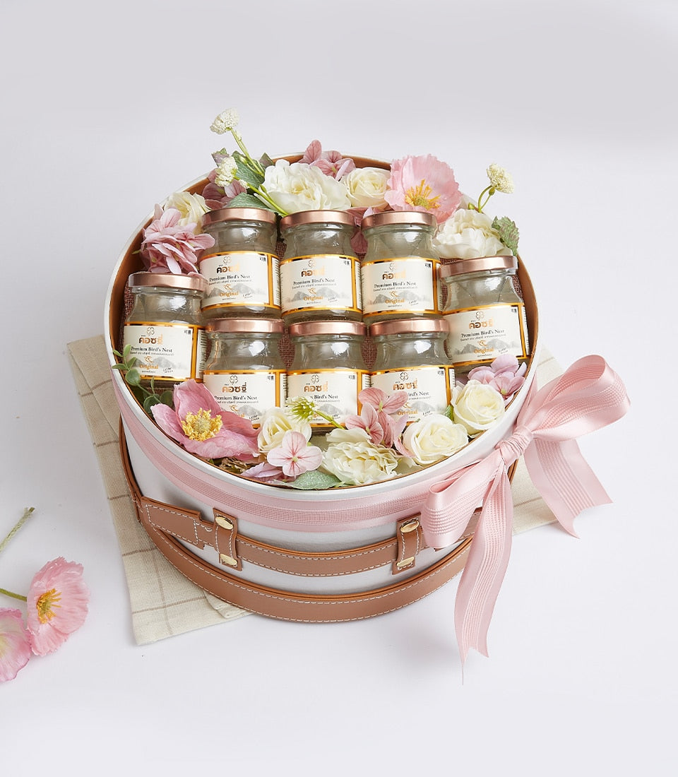 Premium bird's nest gift box with ten glass jars, rose gold lids, and fresh flowers in cream and blush tones