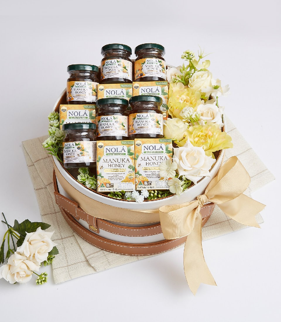 Nola Manuka Honey gift basket with white roses, glass jars, and boxes in white wicker container with gold ribbon