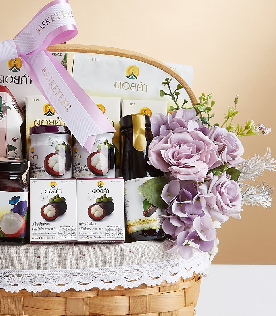 Refined woven gift basket with mangosteen wellness products, purple-lidded jars, dark glass bottle, and lavender flowers