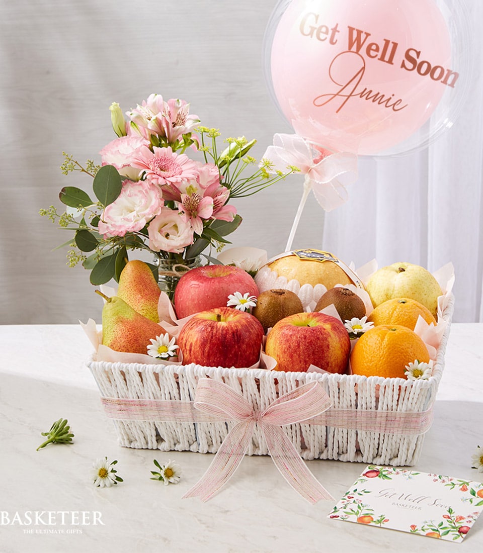 White woven fruit basket with fresh apples, pears, kiwis and citrus, pink-white flowers, and Get Well Soon balloon