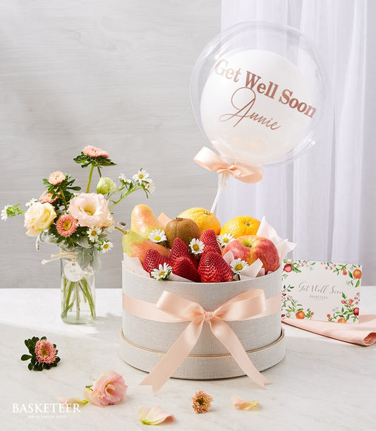 Beige linen fruit basket with strawberries, pears, kiwi, and citrus, paired with personalized bubble balloon and fresh peach