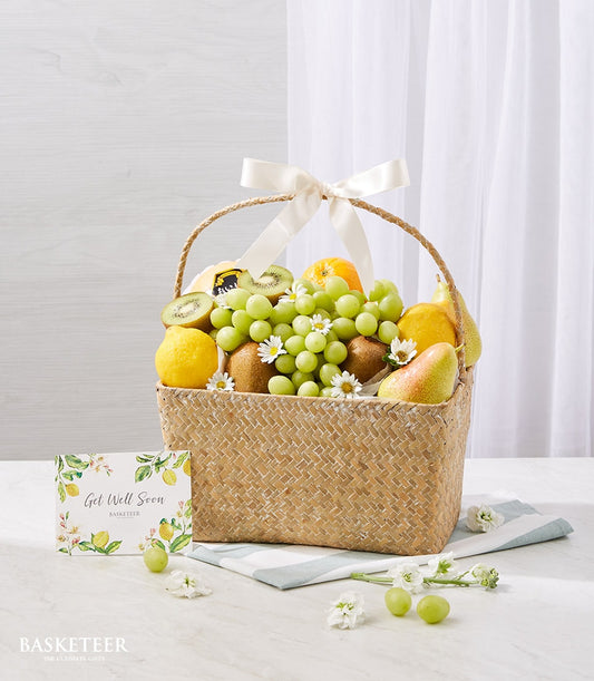 Woven wicker fruit basket with fresh grapes, kiwis, lemons, oranges, pears and white daisies, cream ribbon handle