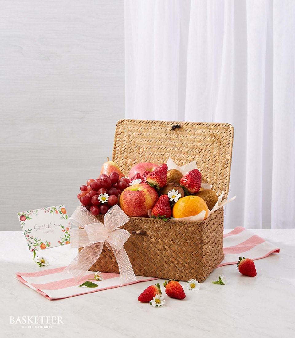 Woven straw fruit basket with red grapes, apples, strawberries, kiwis and orange, tied with pink ribbon