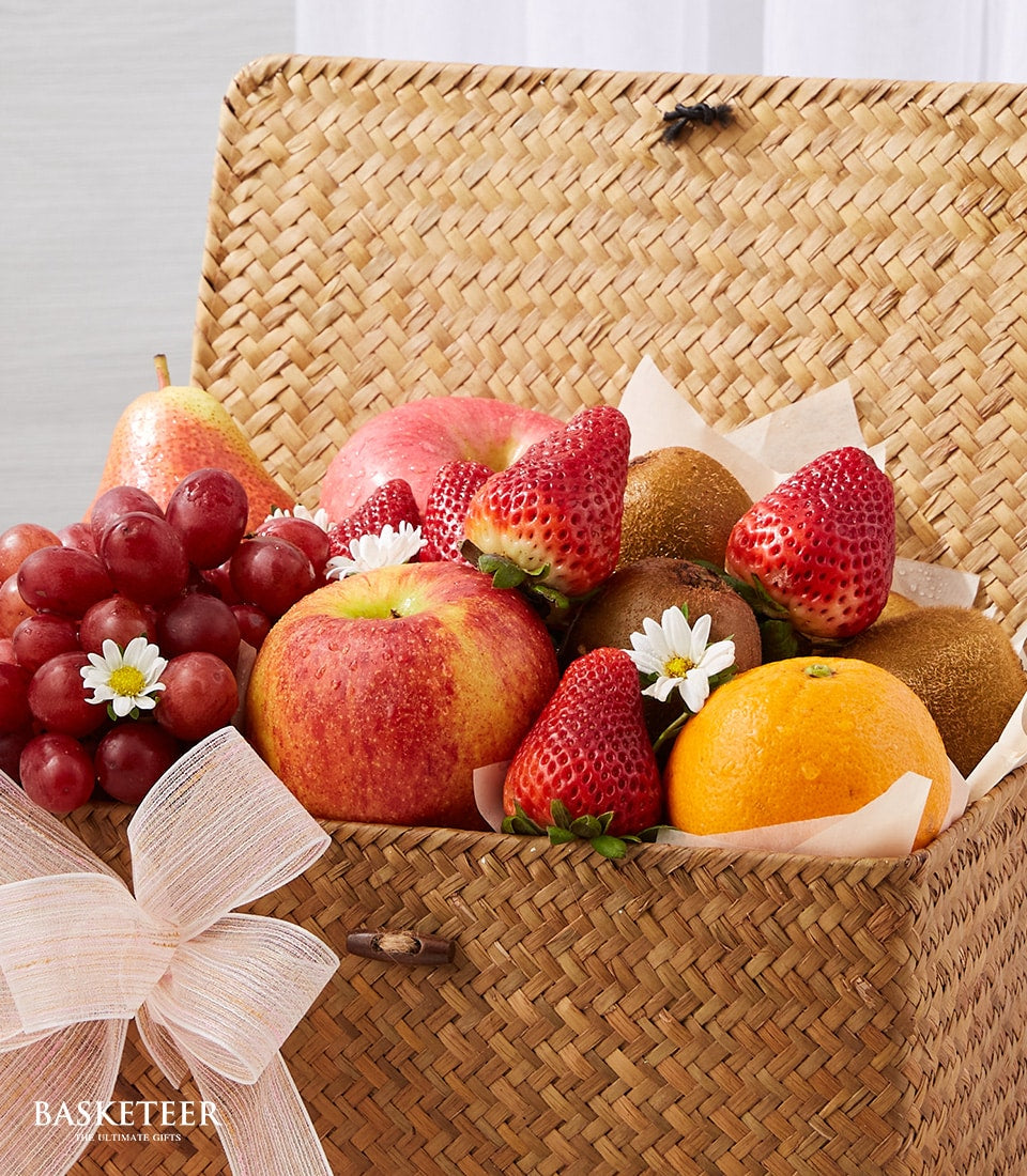 Woven wicker fruit gift basket with fresh grapes, apples, strawberries, kiwi, pear and orange, tied with peach ribbon bow