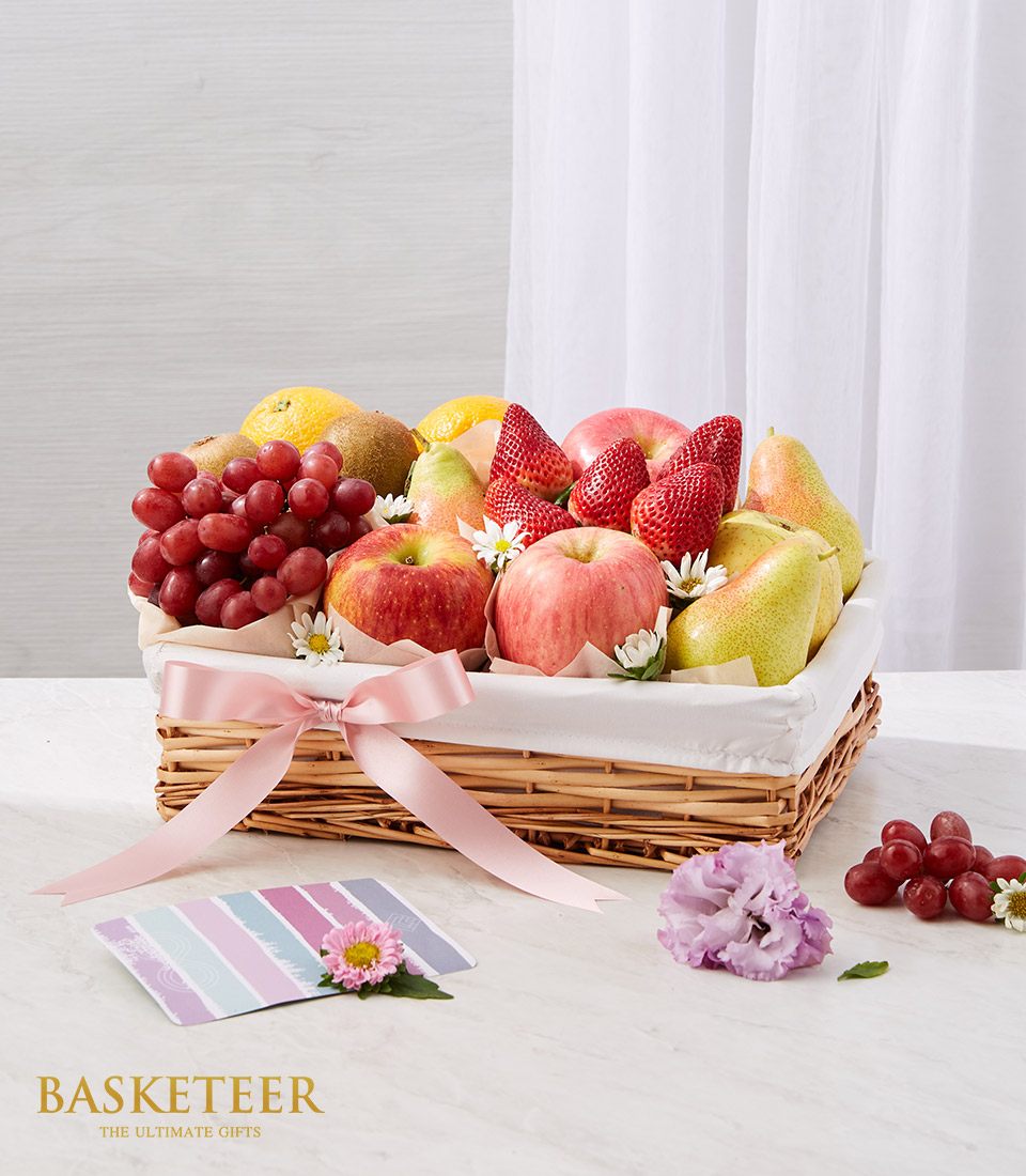 Premium mixed fruit gift basket with red apples, pears, kiwis, and strawberries in woven wicker with pink ribbon bow