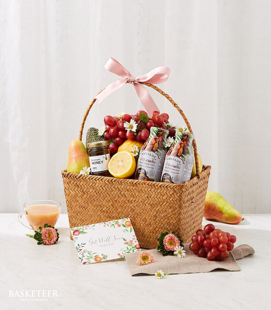 Woven fruit basket with fresh grapes, pear, honey jar, and revitalizing juices tied with pink ribbon for get well recovery
